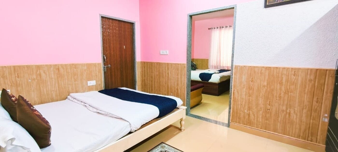 A room with a bed, a wooden wardrobe, and a mirror reflecting another room.