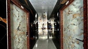 Un couloir aux murs de marbre et au sol réfléchissant, qui mène à un espace central illuminé par des lampes suspendues.
