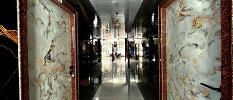 A corridor with marble walls and a reflective floor, leading to a central area with hanging lights.
