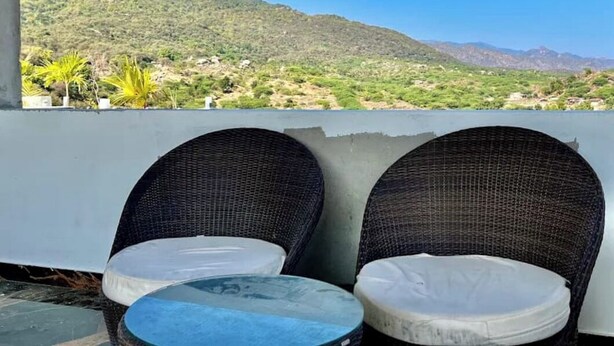 Deux chaises en osier avec des coussins blancs sur une terrasse offrant une vue sur la montagne.