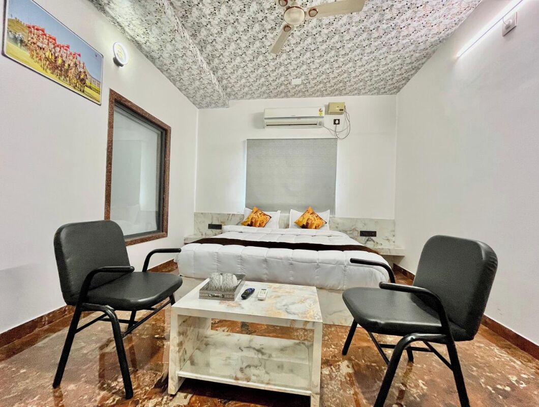 Un dormitorio con cama, dos sillas, una mesita, ventilador de techo y aire acondicionado.