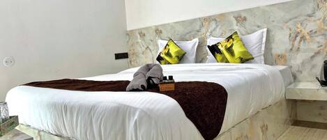 A bed with white bedding, a brown throw blanket, and two pillows with a yellow and black design.