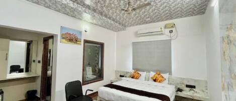 Habitación de hotel con cama, escritorio, silla, espejo y aire acondicionado.