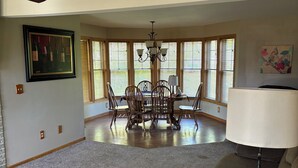 A spacious living room with a dining area, large windows, and a chandelier.