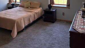 A bedroom with a bed, a ceiling fan, a nightstand, a lamp, a window with curtains, and artwork on the wall.