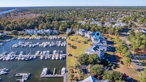 An aerial view of a marina with numerous boats docked, surrounded by residential houses and greenery.
