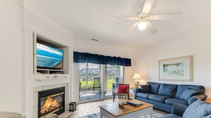 A living room with a fireplace, a television, a sofa, and a ceiling fan.