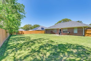 Enjoy a serene backyard retreat with a well-maintained lawn and a shaded area under a large tree.