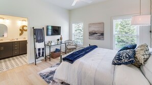 Un dormitorio con cama, televisión, silla, escritorio y ventana.