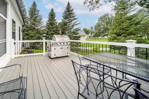 A deck with a grill, outdoor furniture, and a view of trees and houses.