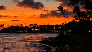 A coastal scene with a sunset, palm trees, and buildings along the shore. - Renee's Poipu Paradise! Oceanfront Views & A/C! (Koloa)