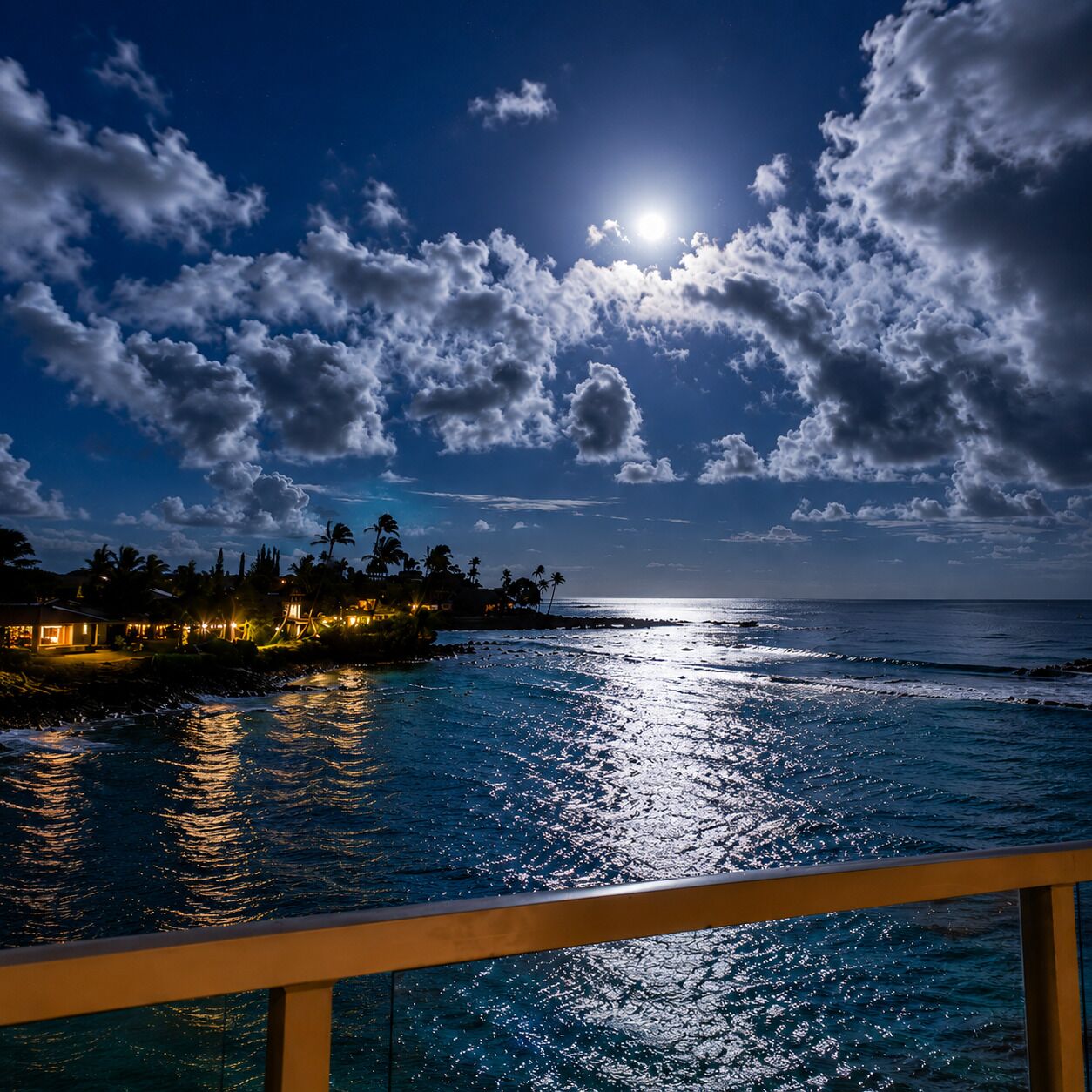 A coastal view with a moonlit sky, ocean waves, and a beachfront property with buildings and palm trees.