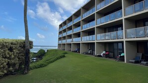 A modern multi-story hotel with balconies, a grassy lawn, and a view of the ocean. - Renee's Poipu Paradise! Oceanfront Views & A/C! (Koloa)