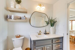 Bathroom features a white toilet, sink, and mirror, with a gold faucet and wooden shelves for storage.