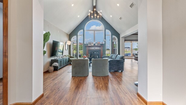 A spacious living room with a high ceiling, a fireplace, and large windows offering a view of the outdoors.