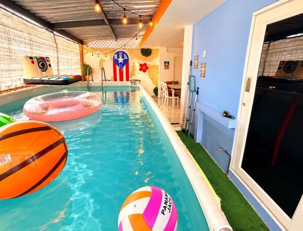 An indoor swimming pool with inflatable toys, a pool ladder, and a wall with a decorative emblem.
