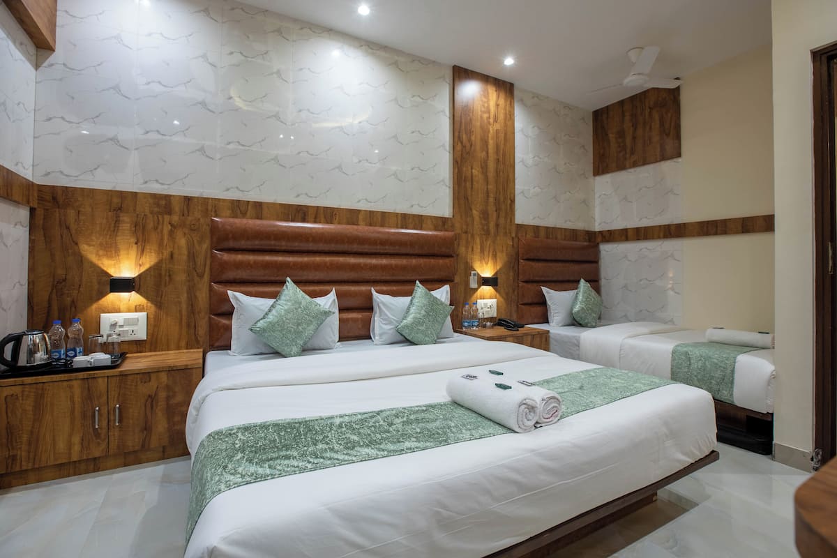 Habitación de hotel con dos camas, cabeceros de madera, paredes con diseño de mármol y almohadones verdes.