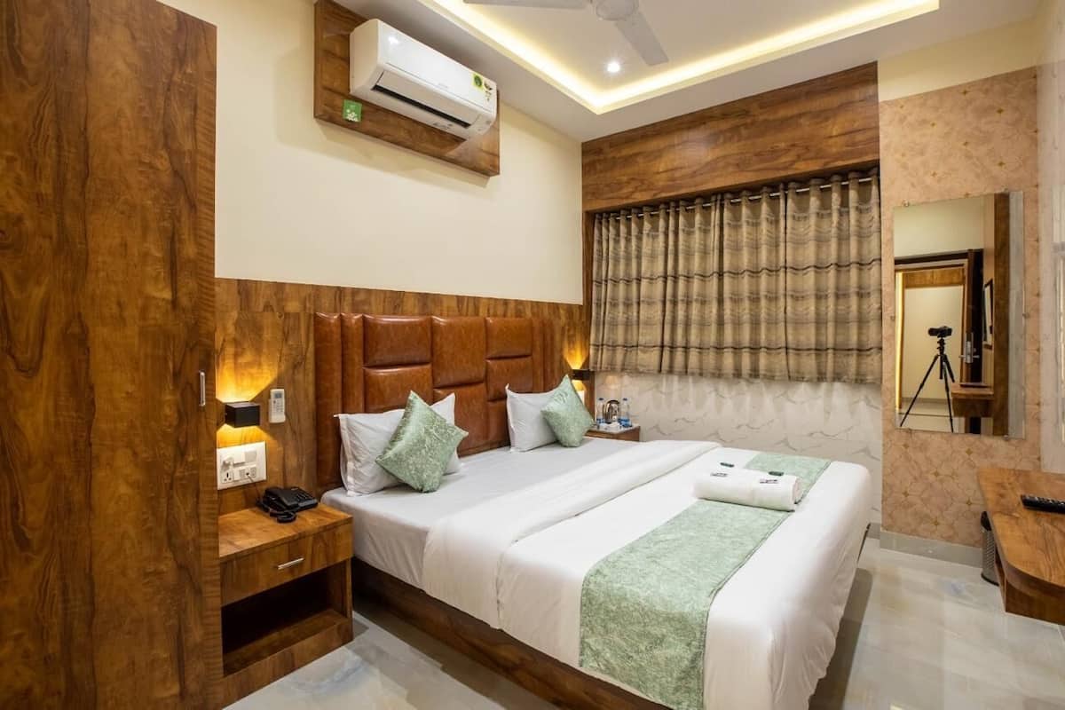 Habitación de hotel con una cama grande, cabecera de madera, lámparas de noche, una mesita de noche, un equipo de aire acondicionado y un espejo con trípode.