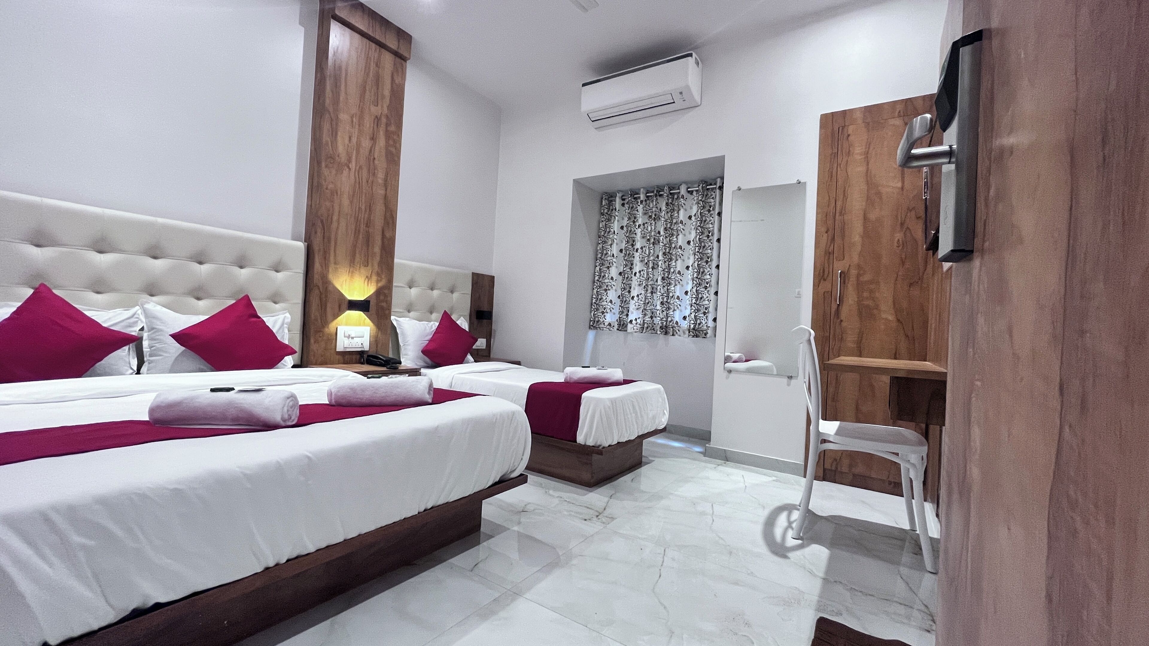 A hotel room with two beds, a wooden headboard, a white upholstered headboard, a mirror, a small table, and a white chair.