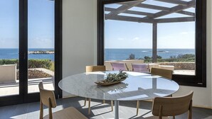 Mesa redonda con sillas en una habitación con ventanas amplias con vista al mar.