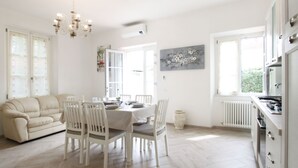 A bright, spacious room with a dining table set for four, a sofa, and a kitchen area with a stove. - Villa Gabriele by Interhome (Forte dei Marmi)