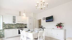 A modern kitchen with white cabinetry, a dining table set for four, and a chandelier. - Villa Gabriele by Interhome (Forte dei Marmi)