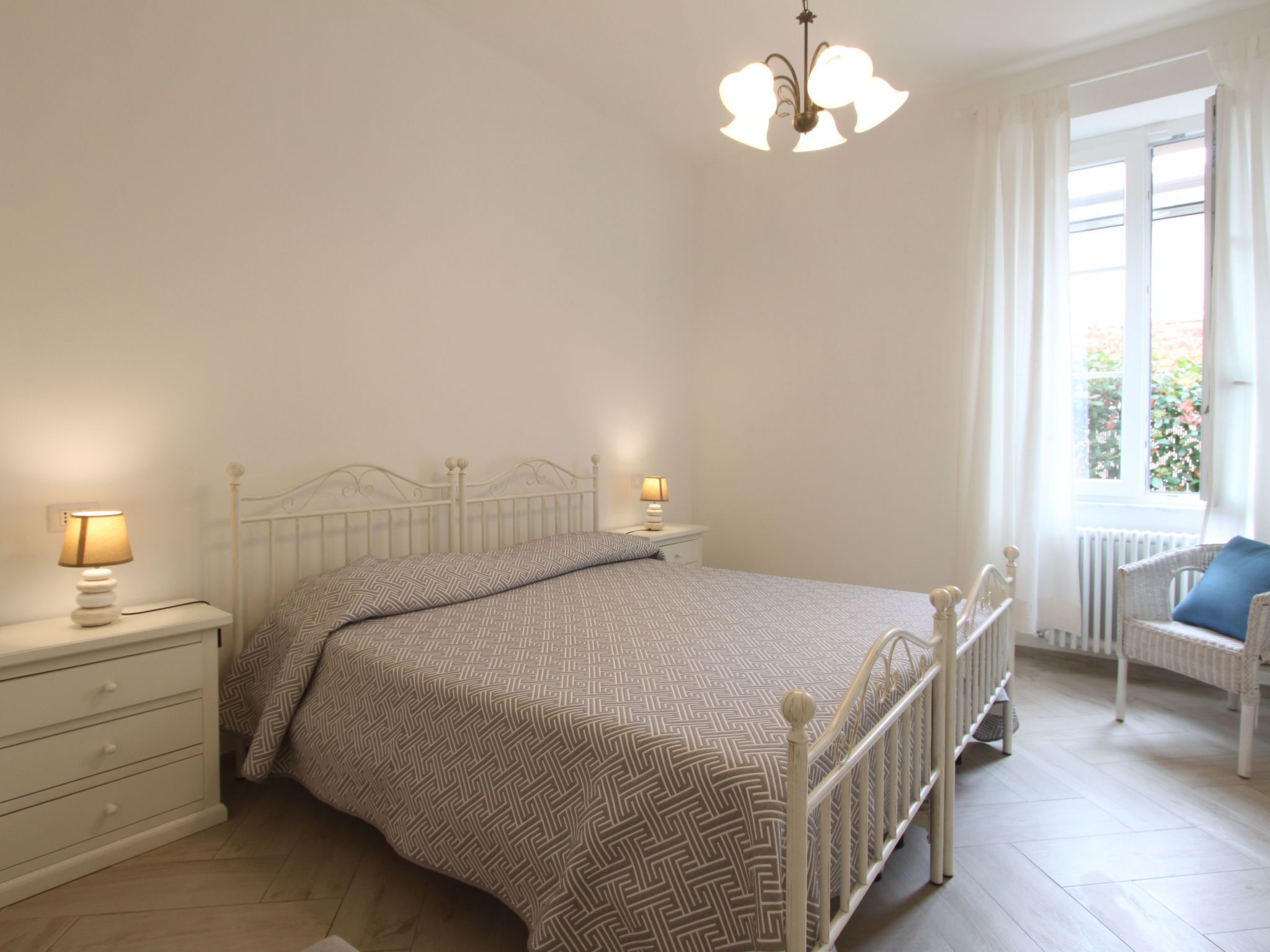 Et soveværelse med seng, sengeborde, lampe, et vindue med gardiner og en stol.