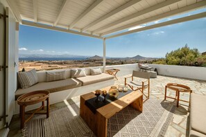 Ein großzügiger Außenbereich mit einer Couch, Sesseln und einem Couchtisch, mit Blick auf eine malerische Landschaft mit Bergen und blauem Himmel.