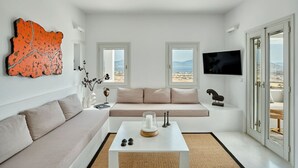 A modern living room with a sofa, a coffee table, and a TV. There are two windows with a view of the landscape. - Villa Inke - Secluded Luxury (Kostos)