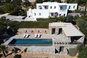 Eine moderne, weiße Villa mit Swimmingpool, Sitzgelegenheiten im Freien und einem Steinweg.
