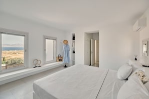 A bedroom with a large bed, a wardrobe, a vanity, and a window with a view of the countryside.