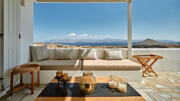 A balcony with a sofa, a wooden chair, and a table with drinks and a jar. - Villa Inke - Secluded Luxury (Kostos)