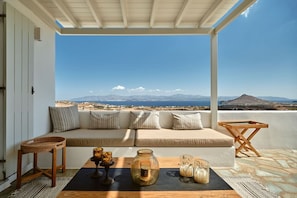 A balcony with a sofa, a wooden chair, and a table with drinks and a jar.