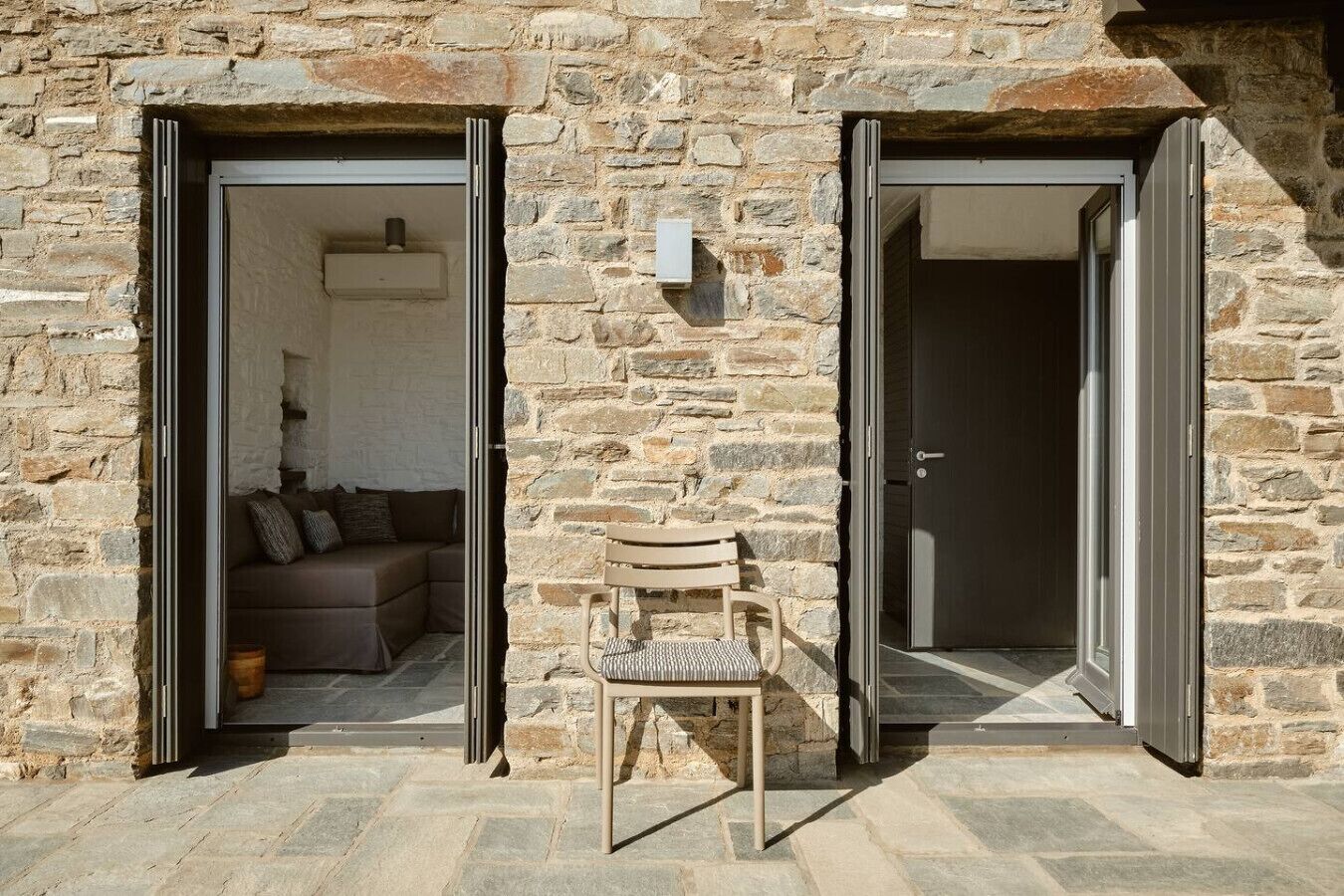 A stone building with two open doors leading to a living area with a sofa and a chair.