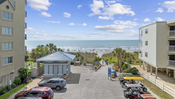 A beachfront property with a parking area, a small building with a blue roof, and a view of the beach and ocean.