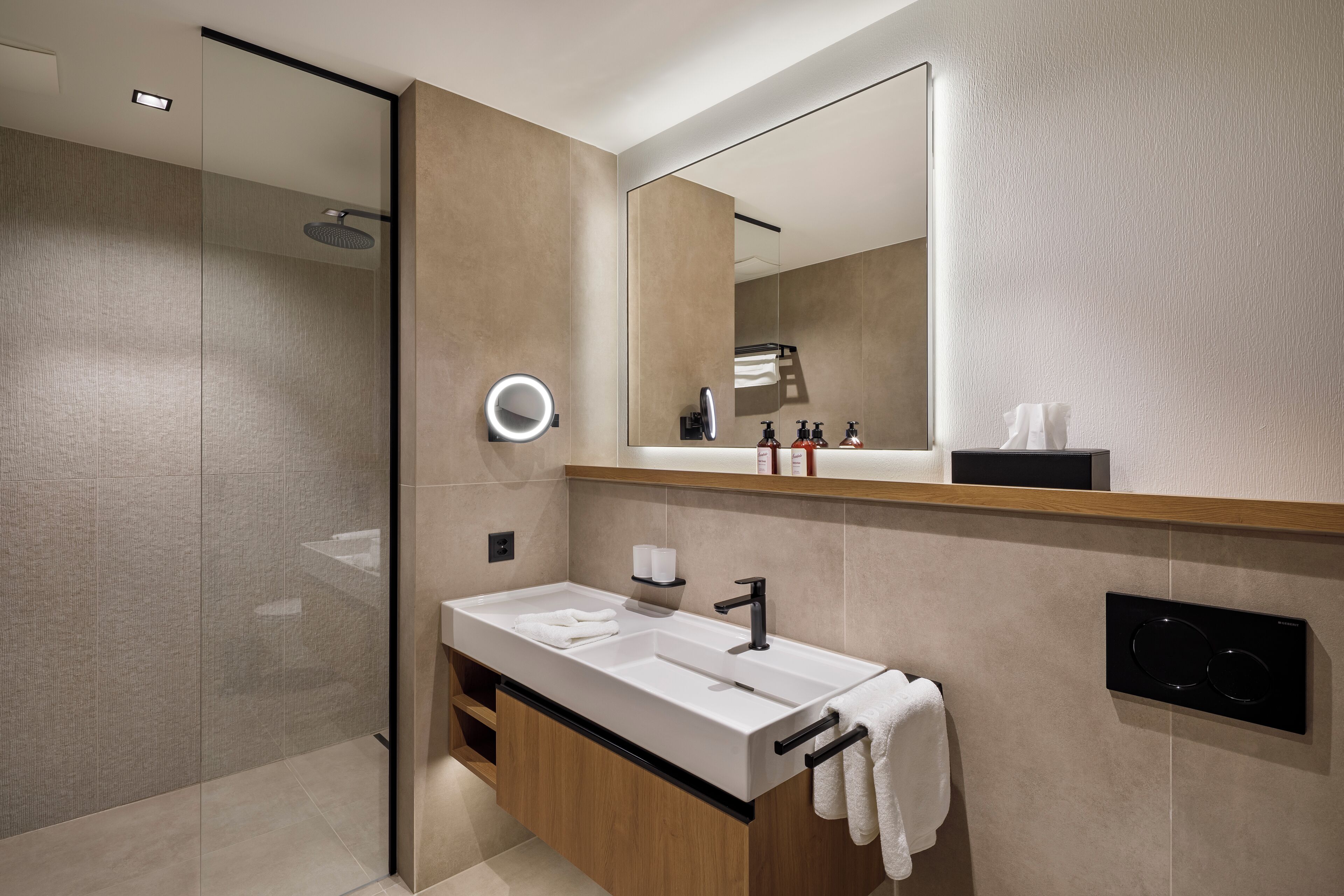 A modern bathroom with a glass shower enclosure, a large mirror, a white sink with a black faucet, and a towel rack.