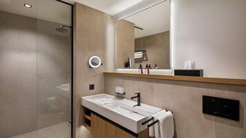 A modern bathroom with a glass shower enclosure, a large mirror, a white sink with a black faucet, and a towel rack.