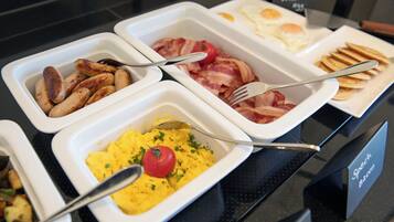 A buffet with various breakfast options including sausages, bacon, eggs, pancakes, and scrambled eggs.