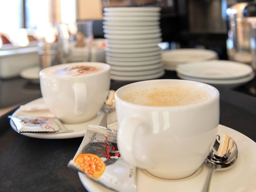 Two white cups of coffee on a tray with a spoon and a packet of creamer.