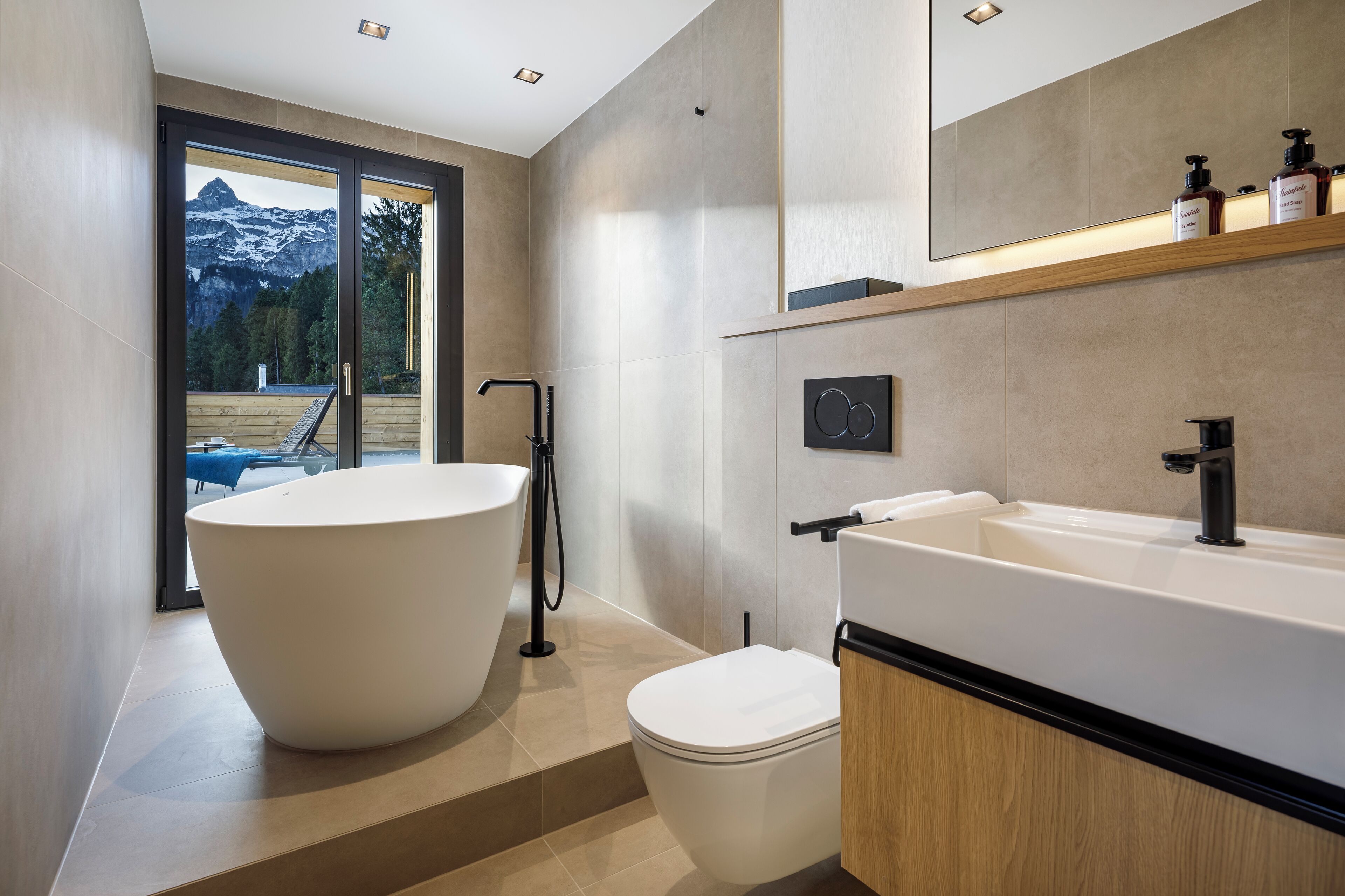 Un baño moderno con una bañera independiente, un inodoro y un espejo grande sobre el lavamanos.