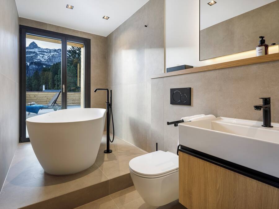 Un baño moderno con una bañera independiente, un inodoro y un espejo grande sobre el lavamanos.