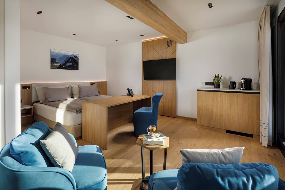 Ein modernes Wohnzimmer mit Sofa, einem kleinen Tisch mit Buch und Tasse, Bett, Wand-Fernseher und einer Küchenzeile mit Arbeitsplatte und Schränken.