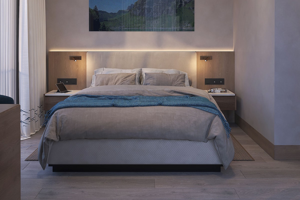Ein modernes Schlafzimmer mit einem großen Bett, zwei Nachttischen, einem Schreibtisch und einem Gemälde einer Berglandschaft.