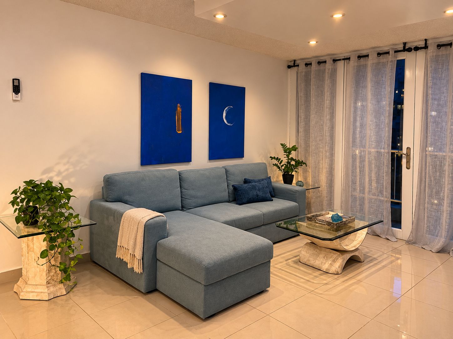 A modern living room with a sectional sofa, a glass coffee table, and two wall-mounted paintings.