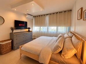 A bedroom with a bed, a dresser, a television, and a window with curtains.