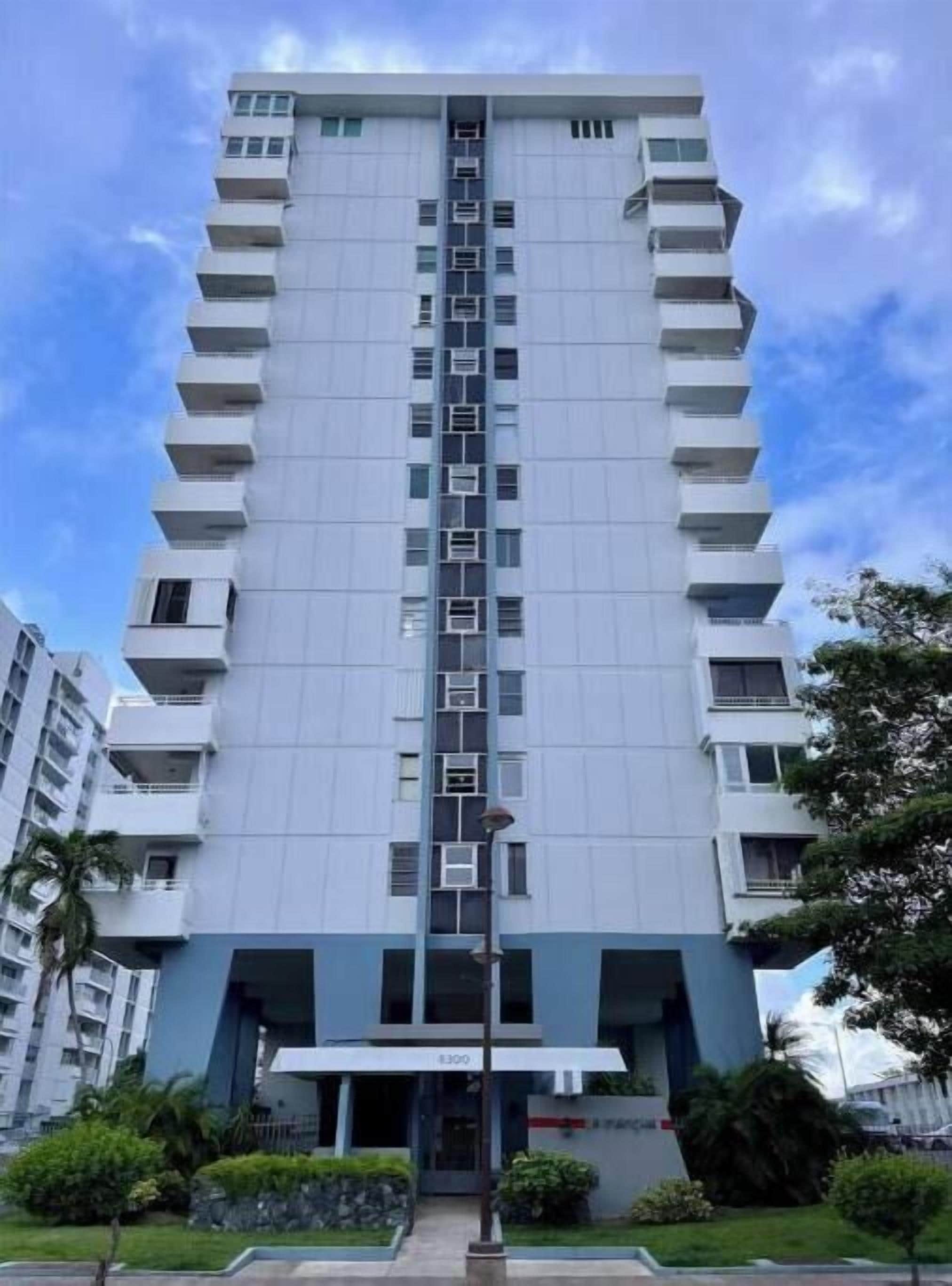 A high-rise building with a central vertical corridor, multiple balconies, and a flat roof.