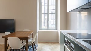 A modern kitchen with a large window, a dining area with a wooden table and white chairs, and a built-in oven. - Elegant Family Apartment in Como centre (Como)