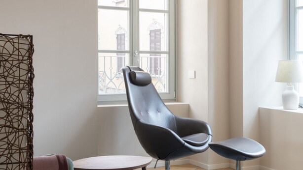 A modern room with a large window, a black leather chair, a small round table, and a white lamp. - Elegant Family Apartment in Como centre (Como)