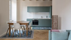 A modern kitchen with teal cabinets, a dining table with chairs, and a patterned rug. - Elegant Family Apartment in Como centre (Como)