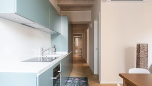 A narrow hallway with a kitchen on one side, featuring a sink and cabinets. A wooden table and a chair are visible on the right. - Elegant Family Apartment in Como centre (Como)